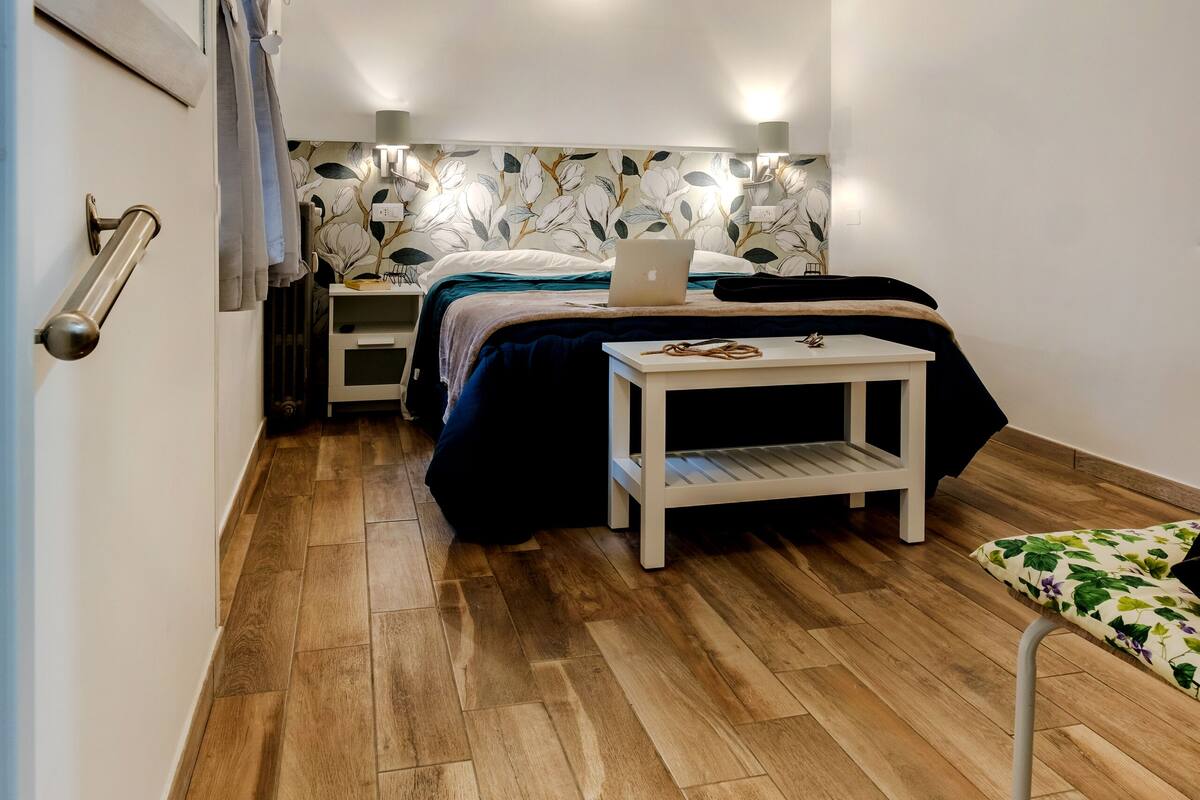 A compact room with a bed, bedside table, and a laptop.