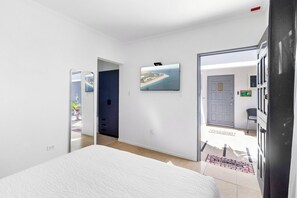 A bedroom with a bed, a door leading to a balcony, and a wall-mounted TV. - Charming 1BR w/ Shared Pool, near Aruba’s Beaches (Noord)