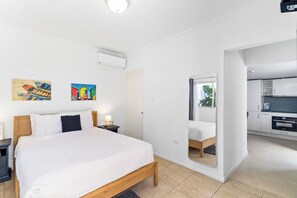 A bedroom with a bed, bedside table, and a nightstand. There is a mirror on the wall, and a door leading to a bathroom.