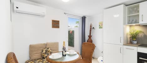 A compact living space with a kitchenette, a dining area with wicker furniture, a sofa with patterned cushions, and a door leading to an outdoor area.