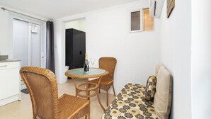 Un espacio habitable compacto con kitchenette, una zona de comedor con mobiliario de mimbre y un sofá con cojines estampados.