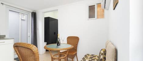 Un espace de vie compact comprenant un coin cuisine, un coin repas avec des meubles en osier et un canapé agrémenté de coussins à motifs.