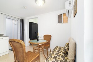 A compact living space with a kitchenette, a dining area with wicker furniture, and a sofa with patterned cushions. - Charming 1BR w/ Shared Pool, near Aruba’s Beaches (Noord)