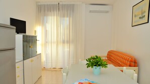 A compact room with a dining table, a sofa, a TV on a cabinet, and a potted plant. - Bibione Pineta Family Retreat (San Michele al Tagliamento)