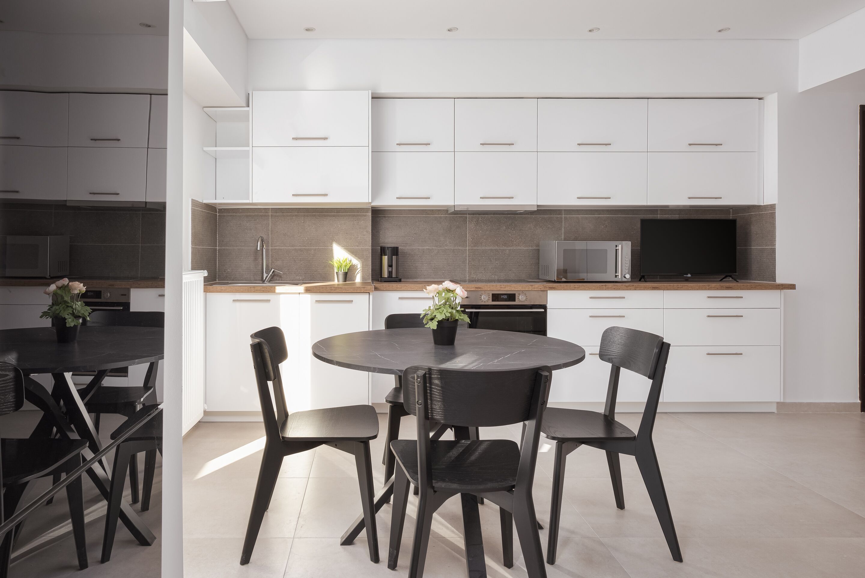 A modern kitchen with white cabinets, a round dining table, and black chairs.