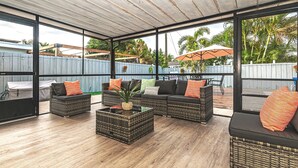 An outdoor patio with wicker furniture, a central coffee table, and a view of the backyard.