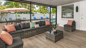 A sunlit patio with wicker furniture, a pool, and a view of a backyard.