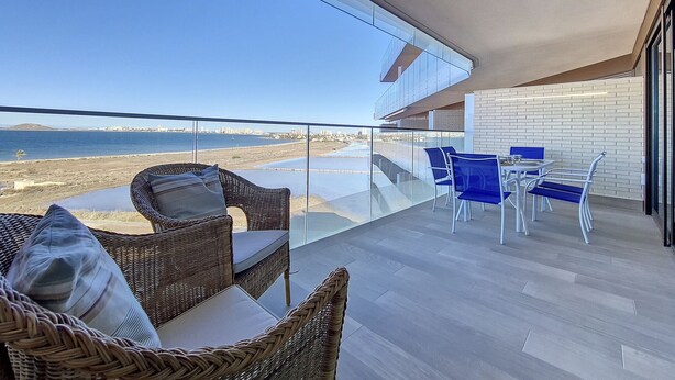 Un balcon doté de meubles en osier et d’une table, offrant une vue sur la plage et le paysage urbain.