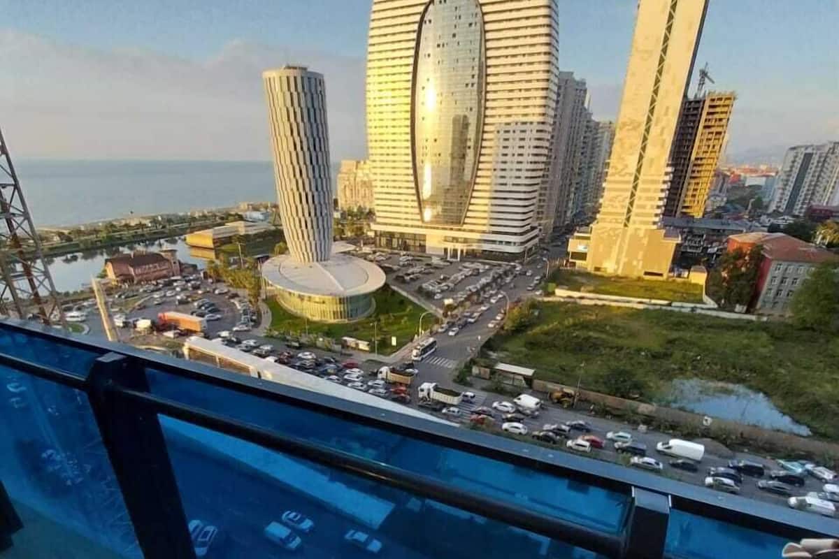 A high-rise building with a distinctive circular design, surrounded by other modern structures and a busy road with vehicles.