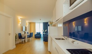A modern kitchen with a built-in stove, a dining area with blue chairs, and a living space with a sofa and a coffee table. - Holiday Point Orbi City (Batumi)