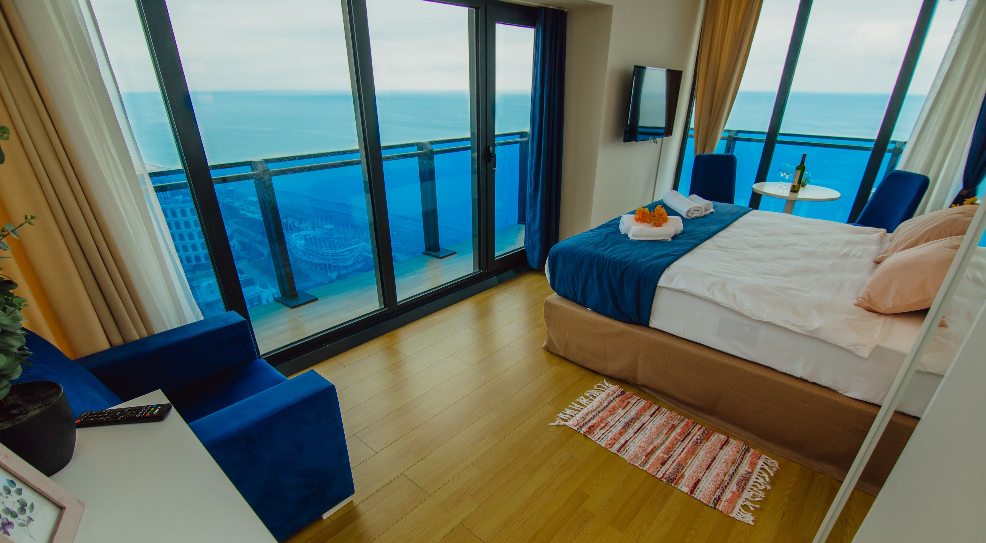 A hotel room with a balcony, a bed, a desk, and a view of the sea.