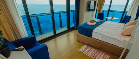 Habitación de hotel con balcón, cama, escritorio y vista al mar.