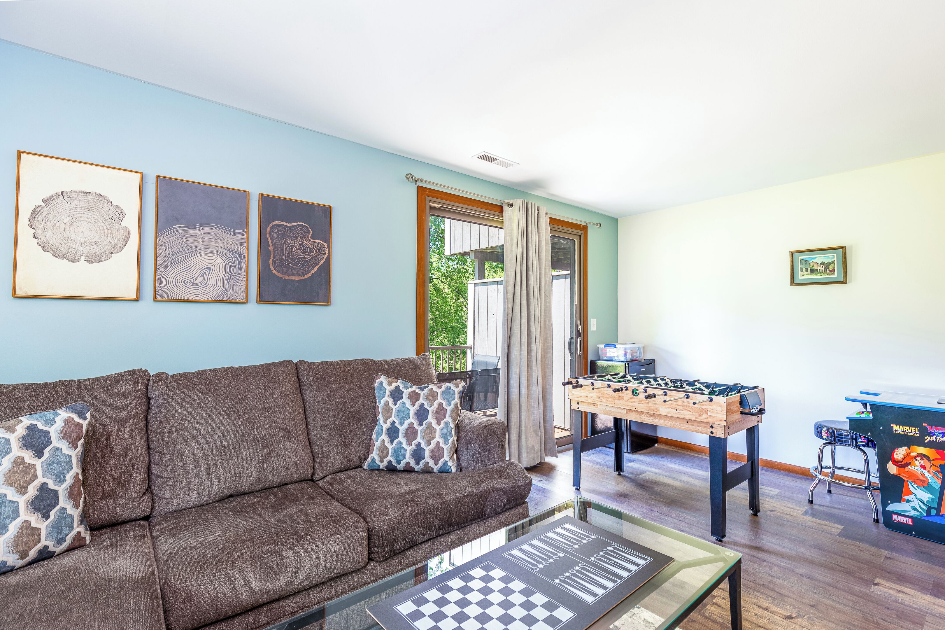 A living room with a brown sofa, a foosball table, and framed artwork on the wall.