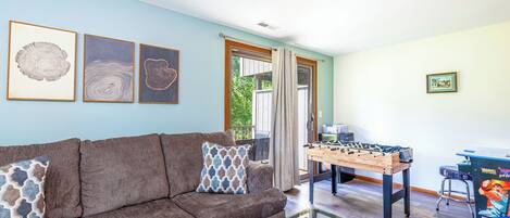 A living room with a brown sofa, a foosball table, and framed artwork on the wall.