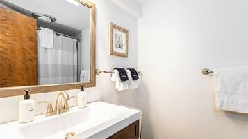 A bathroom with a white sink, gold faucets, and a large mirror. There are two towels hanging on a towel rack, one white and one with "MANUEL" on it.