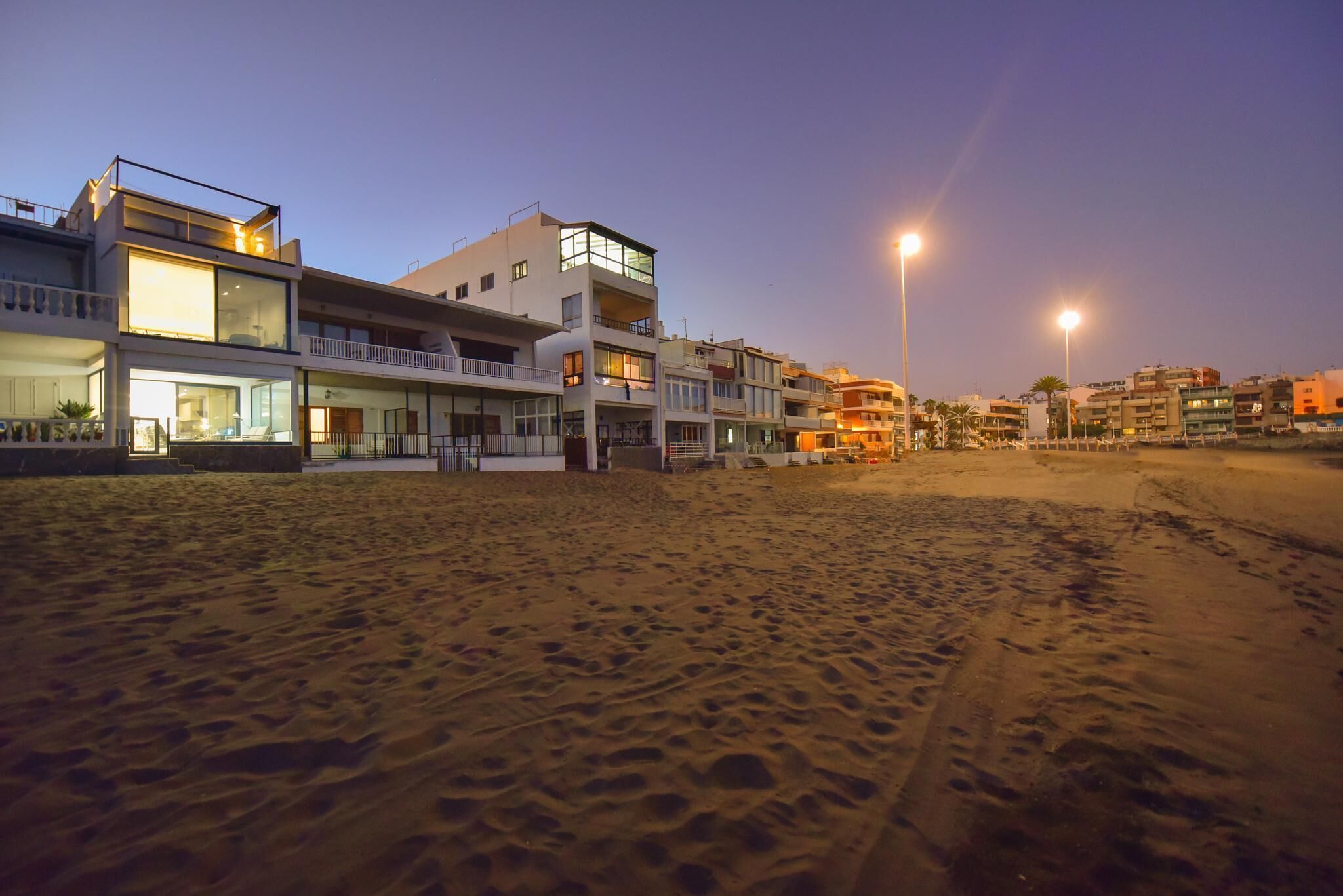Un hotel frente a la playa con varios balcones, amplias ventanas y una playa arenosa al frente.