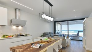A modern kitchen with a wooden dining table, white chairs, and a view of the ocean through large windows. - La Terraza de Salinetas By VillaGranCanaria (Telde)