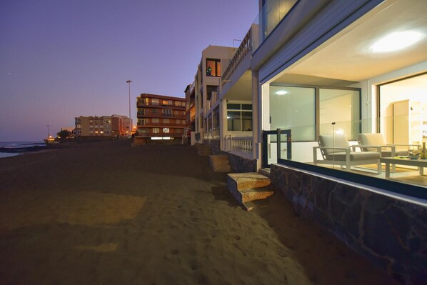 A beachfront hotel with a stone facade, large windows, and a balcony overlooking the beach.