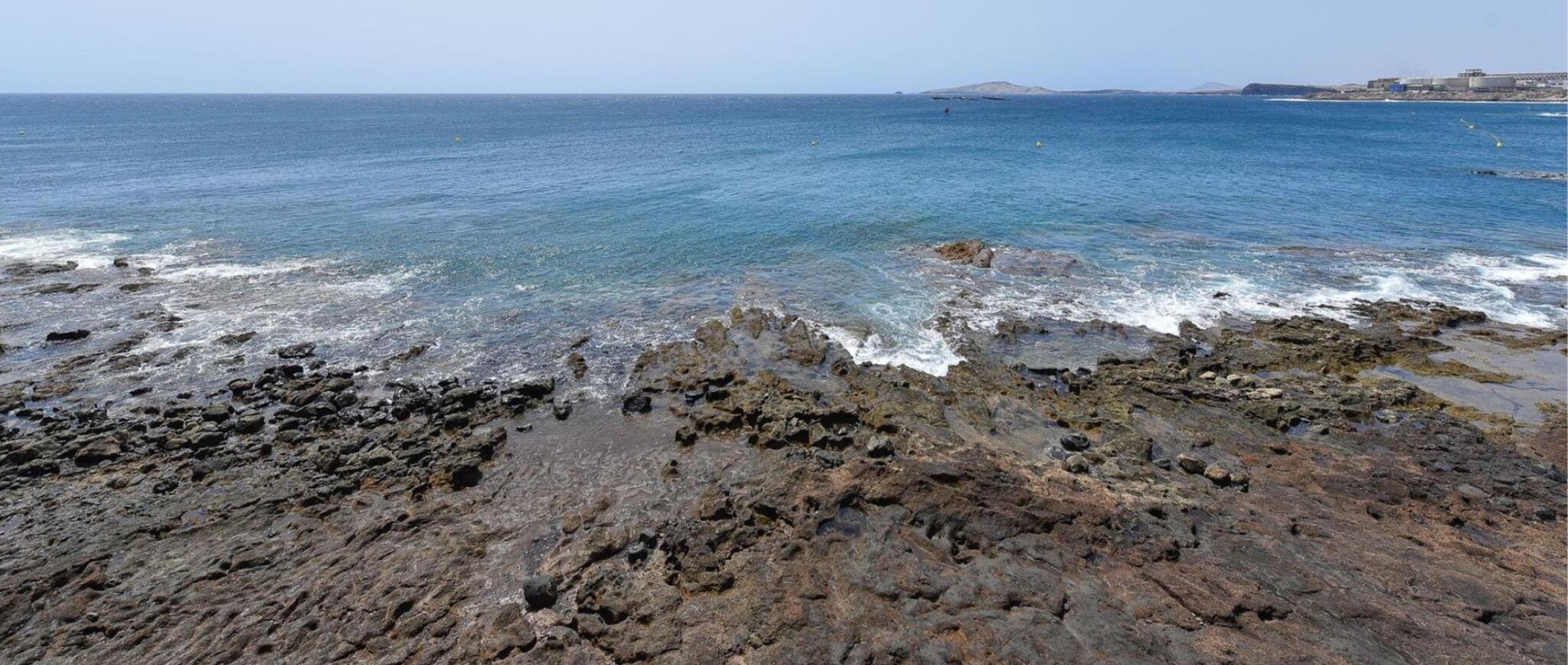 Eine felsige Küstenlinie mit klarem, blauem Wasser und weiter Blick auf das Land.