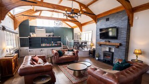 A spacious living room with leather sofas, a fireplace, a stone wall, and a kitchen in the background.