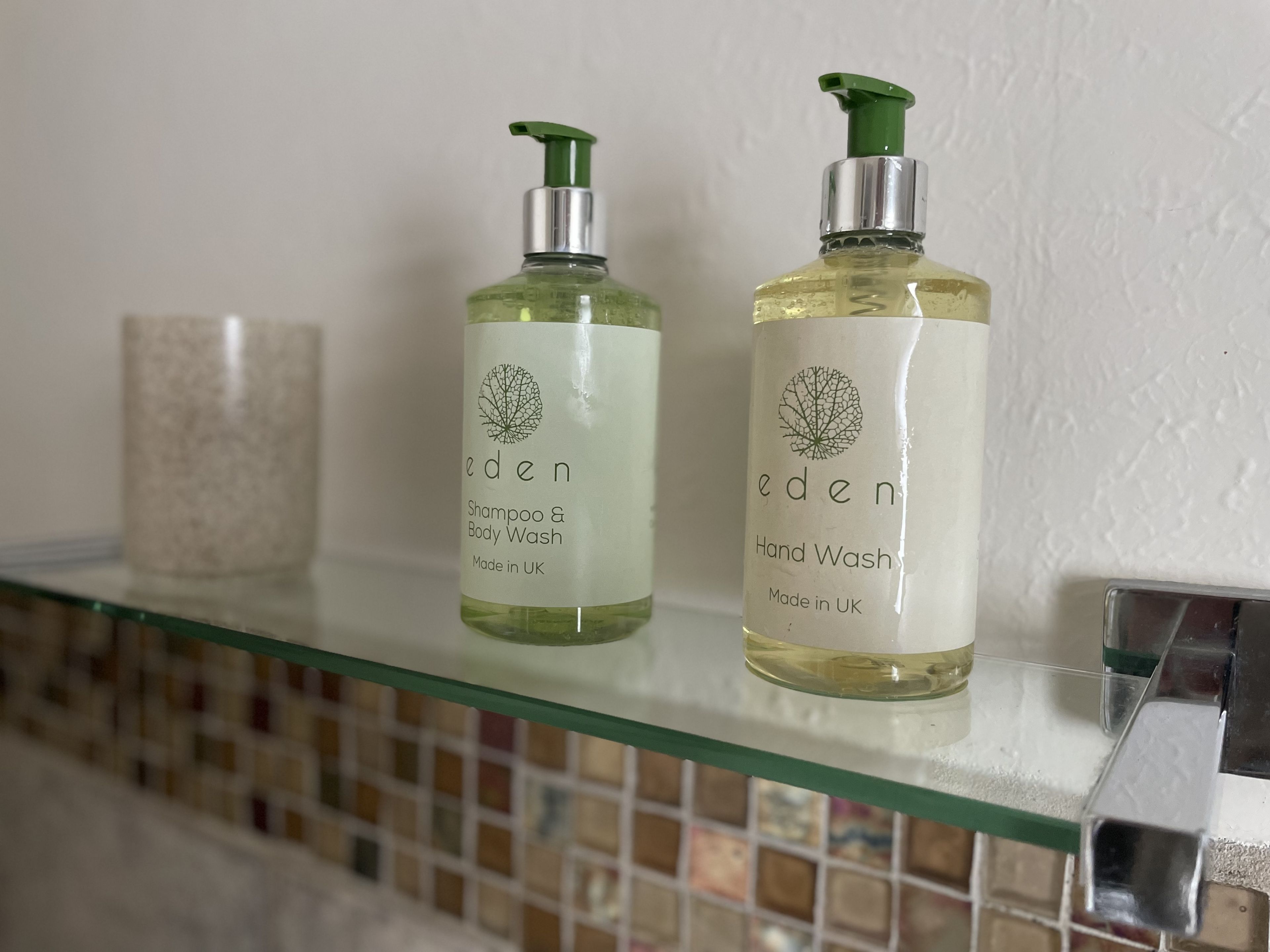 Deux flacons de savon pour les mains et de shampoing de la marque Eden, posés sur une étagère en verre.