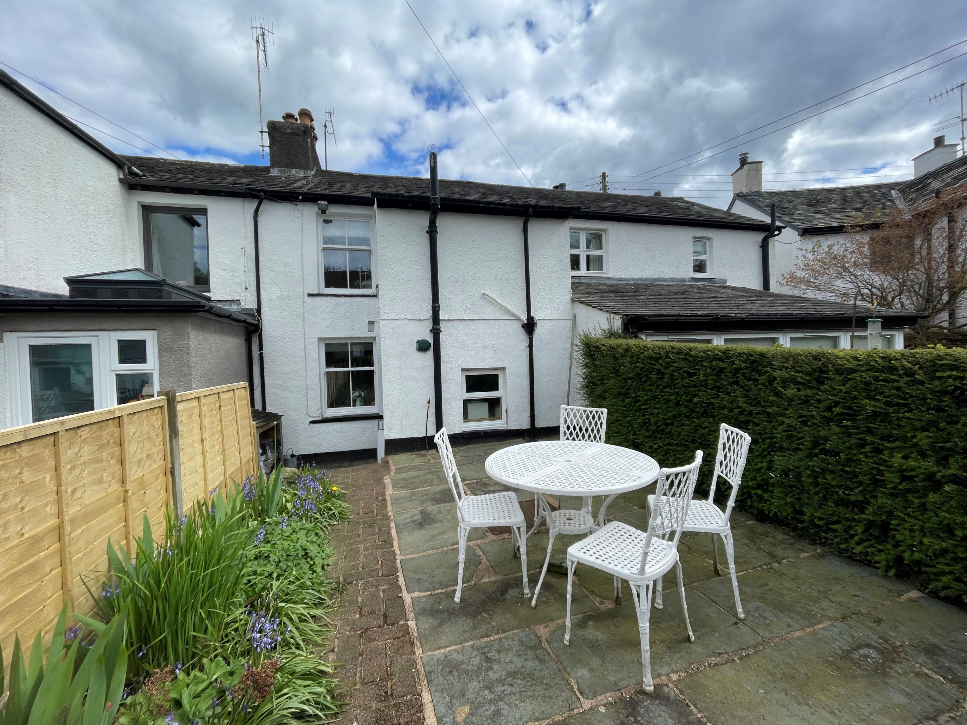 Une maison blanche dotée d’un patio avec jardin, comprenant une table ronde et des chaises blanches.