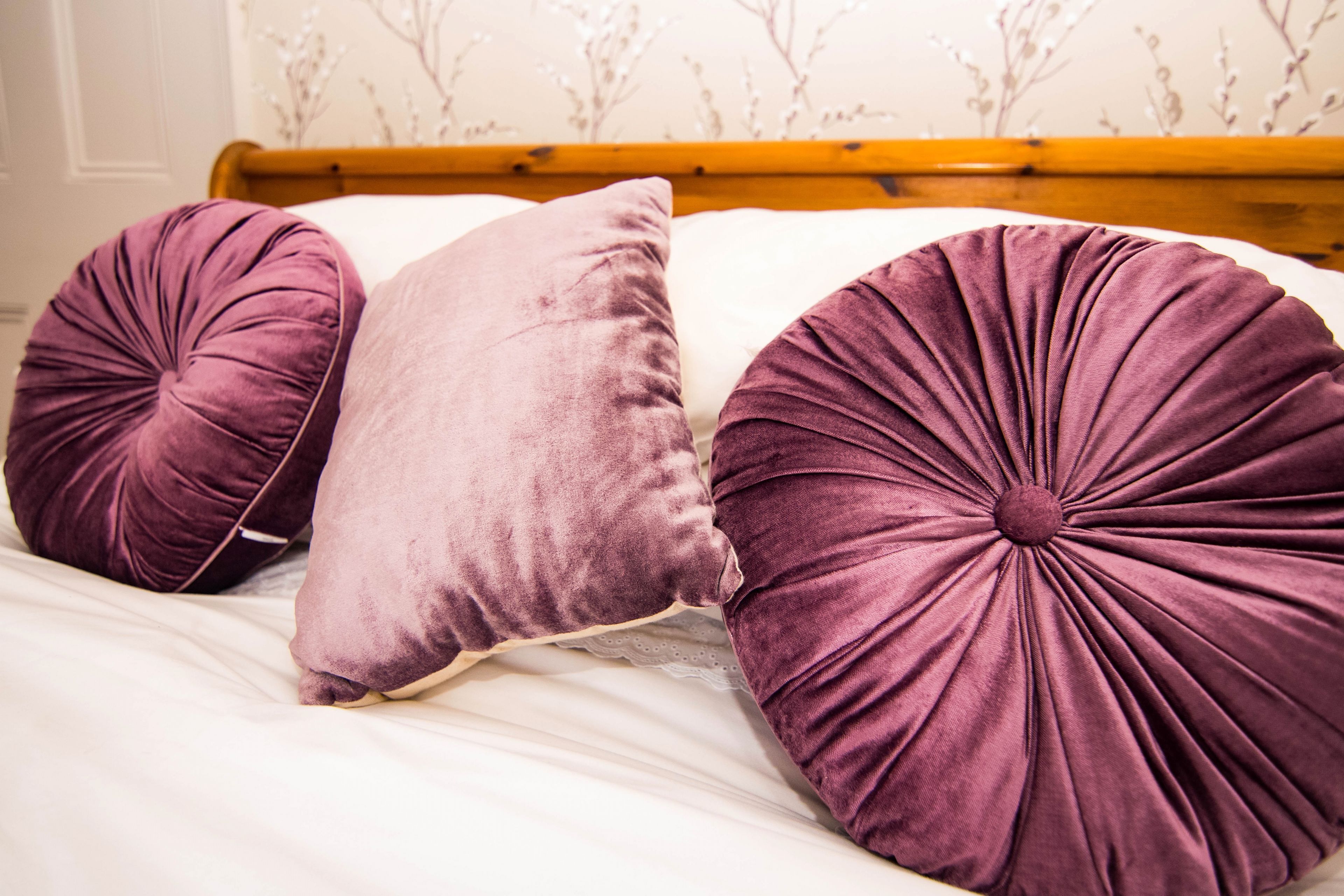 A bed with three large, round, purple pillows and a wooden headboard.