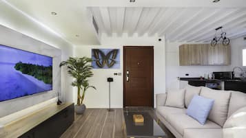 A modern living room with a flat-screen TV, a large potted plant, a sofa with cushions, and a coffee table.