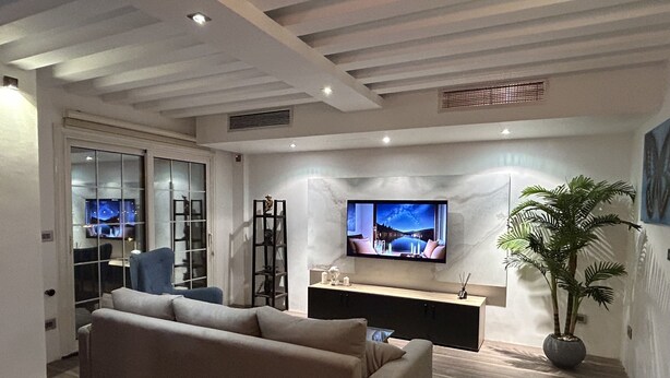 A modern living room with a beige sofa, a TV mounted on the wall, a wooden cabinet, and a potted plant.