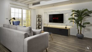 A modern living room with a grey sofa, a blue chair, a TV mounted on the wall, a plant, and a wooden floor.