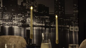 A table set with candles, a glass, and a pitcher, with a cityscape view in the background.