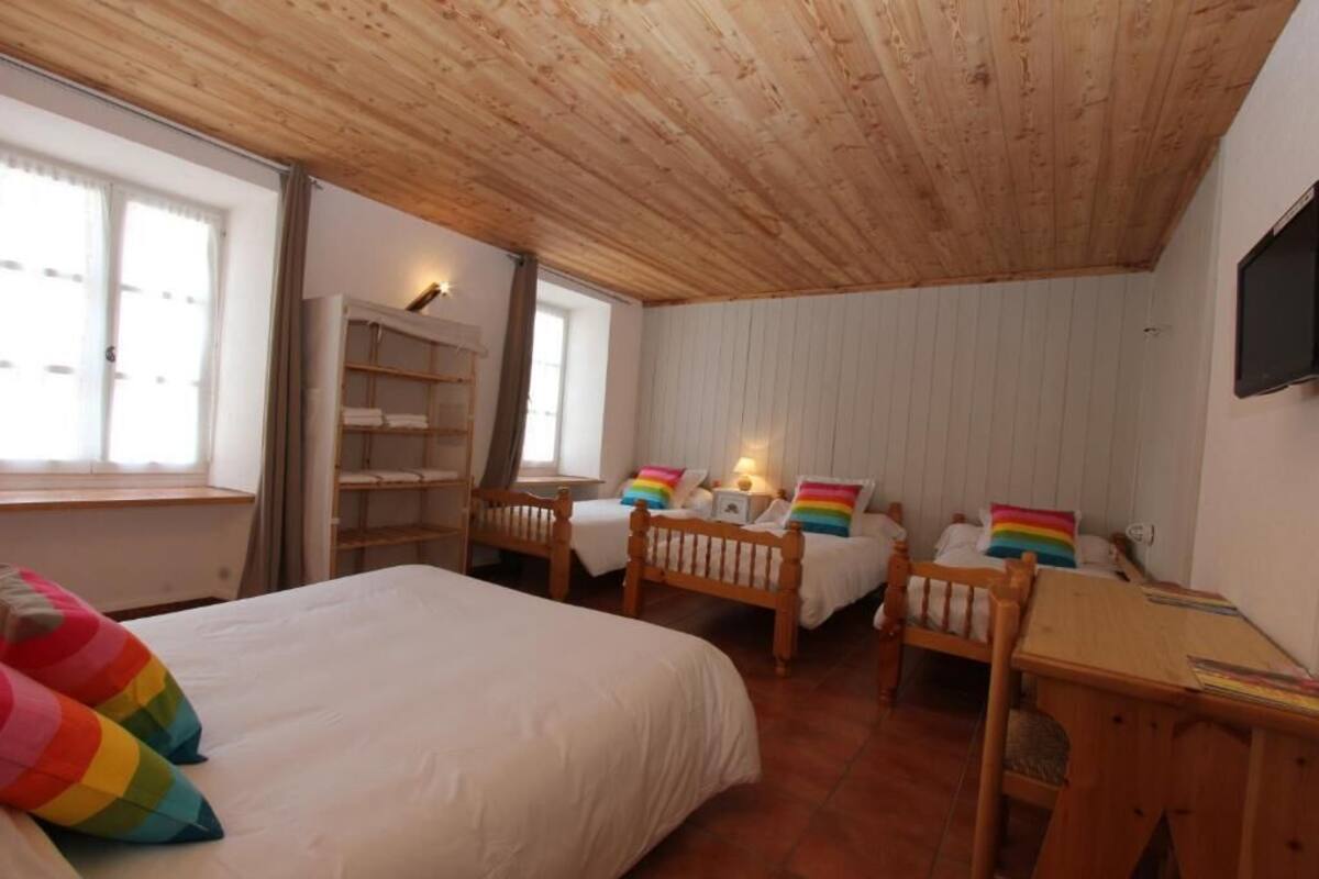 Un dormitorio con una cama grande, dos camas más pequeñas, muebles de madera, un televisor y una ventana con cortinas.
