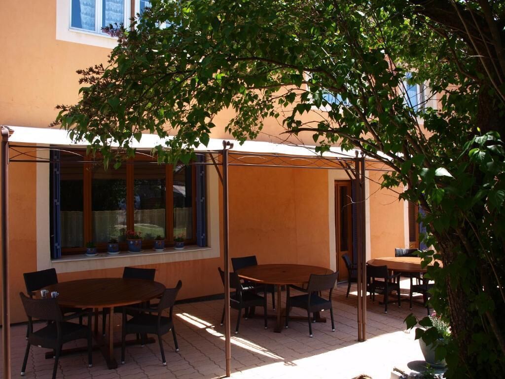 Un espacio de patio al aire libre con mesas y sillas redondas, una zona de estar cubierta y plantas en macetas.