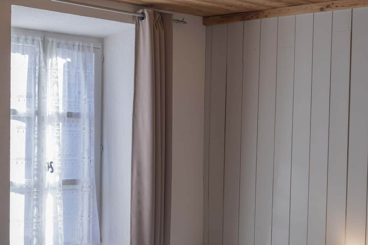 Un dormitorio con dos camas, cabeceros de madera, una ventana con cortinas y una lámpara de noche.