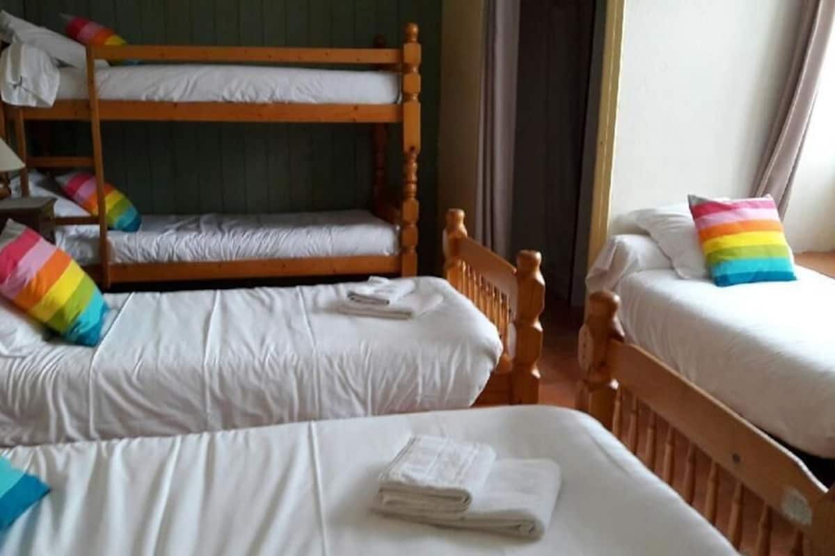 Una habitación con dos literas, cada una con un colchón blanco y almohadas de colores. Hay una mesita con una lámpara y una silla.