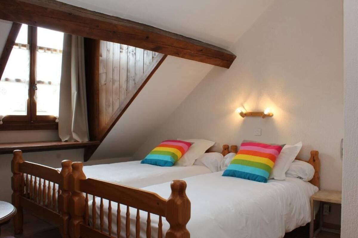Un dormitorio con dos camas, cabeceros de madera, una ventana con cortinas y una lámpara fijada a la pared.