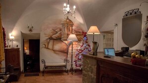 Un intérieur chaleureux, éclairé d’une lumière douce, avec une cheminée en pierre, un lustre et une fresque murale.