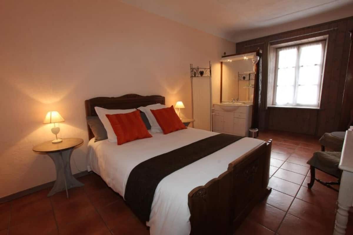 Una habitación de hotel con cama, mesitas de noche, un espejo, una ventana y un baño.