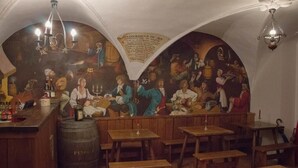 Un espace bar avec des tables et des bancs en bois, un grand tonneau et une fresque représentant des scènes historiques.