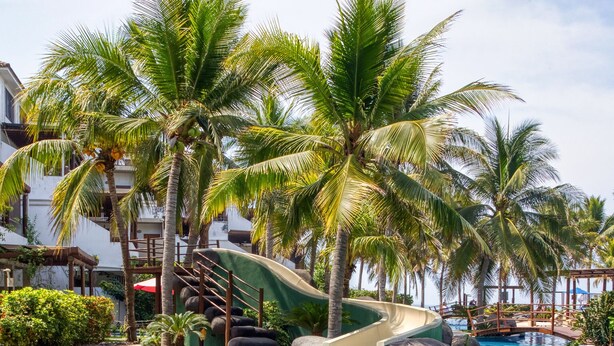 A swimming pool with clear blue water, surrounded by palm trees and a small waterfall. - DELUXE PENTHOUSE VILLA THE PALMS (El Gariton)