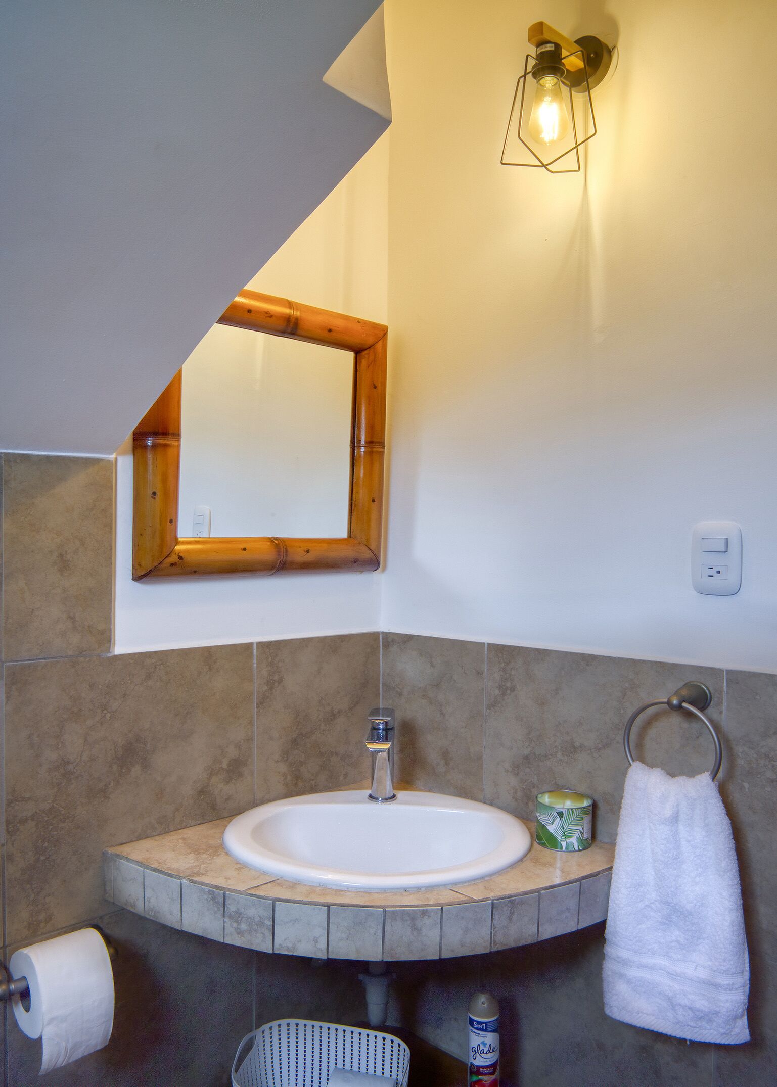 A bathroom with a white sink, a wooden-framed mirror, a towel ring, and a wall-mounted light fixture.