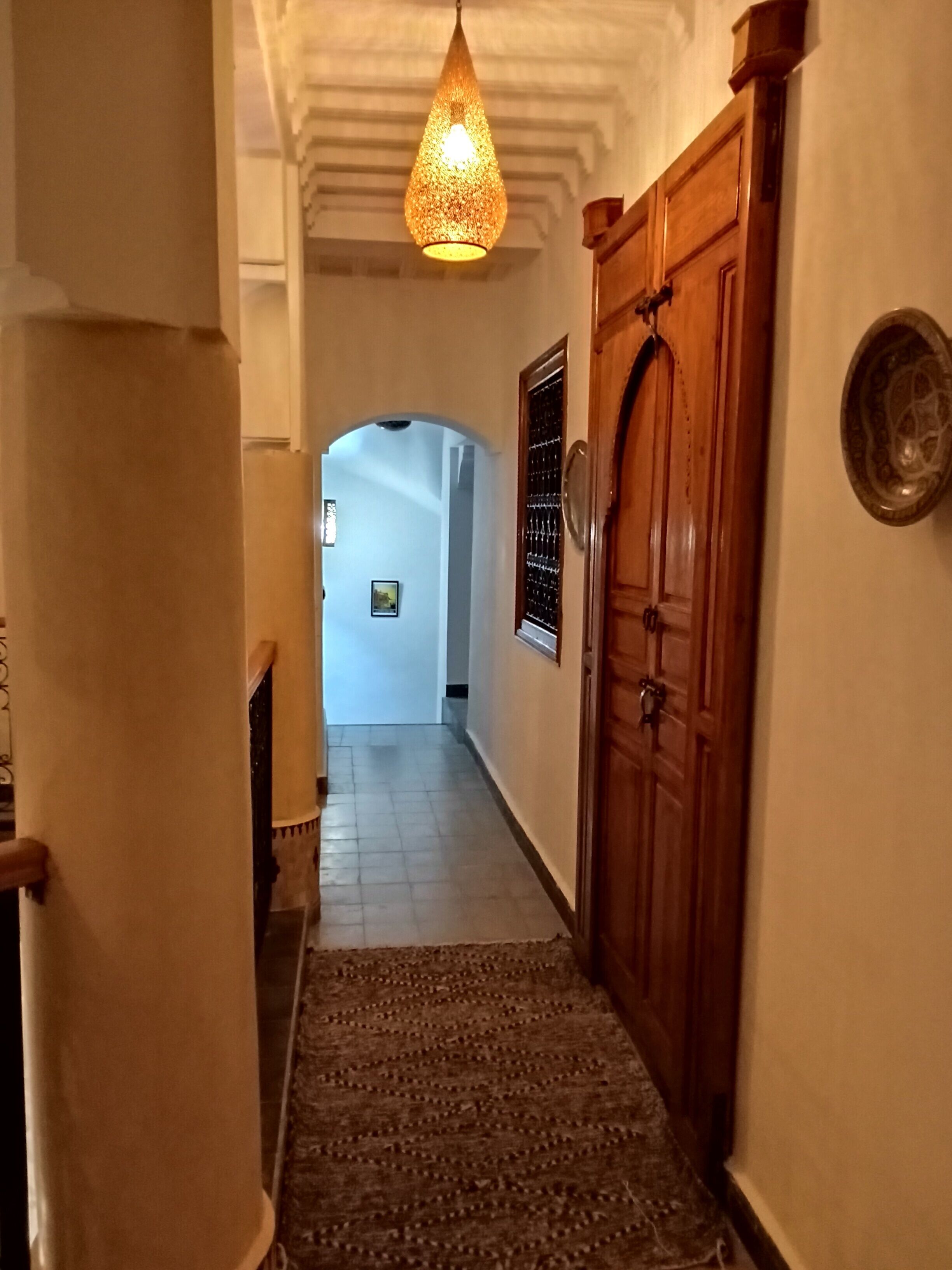 A hallway with a patterned rug, a wooden door, and a hanging light fixture.