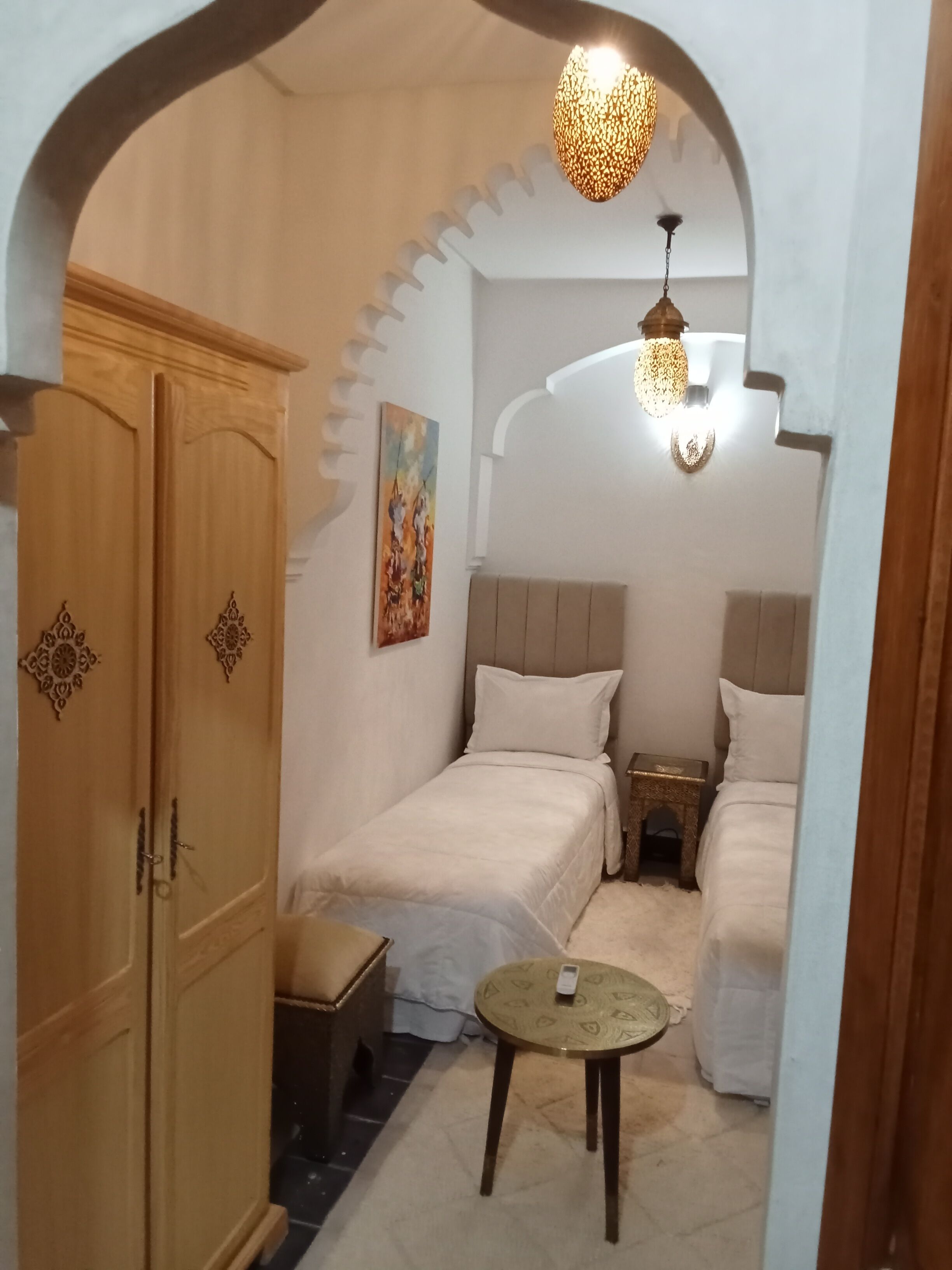 Quarto compacto com duas camas, uma mesinha e um guarda-roupa.