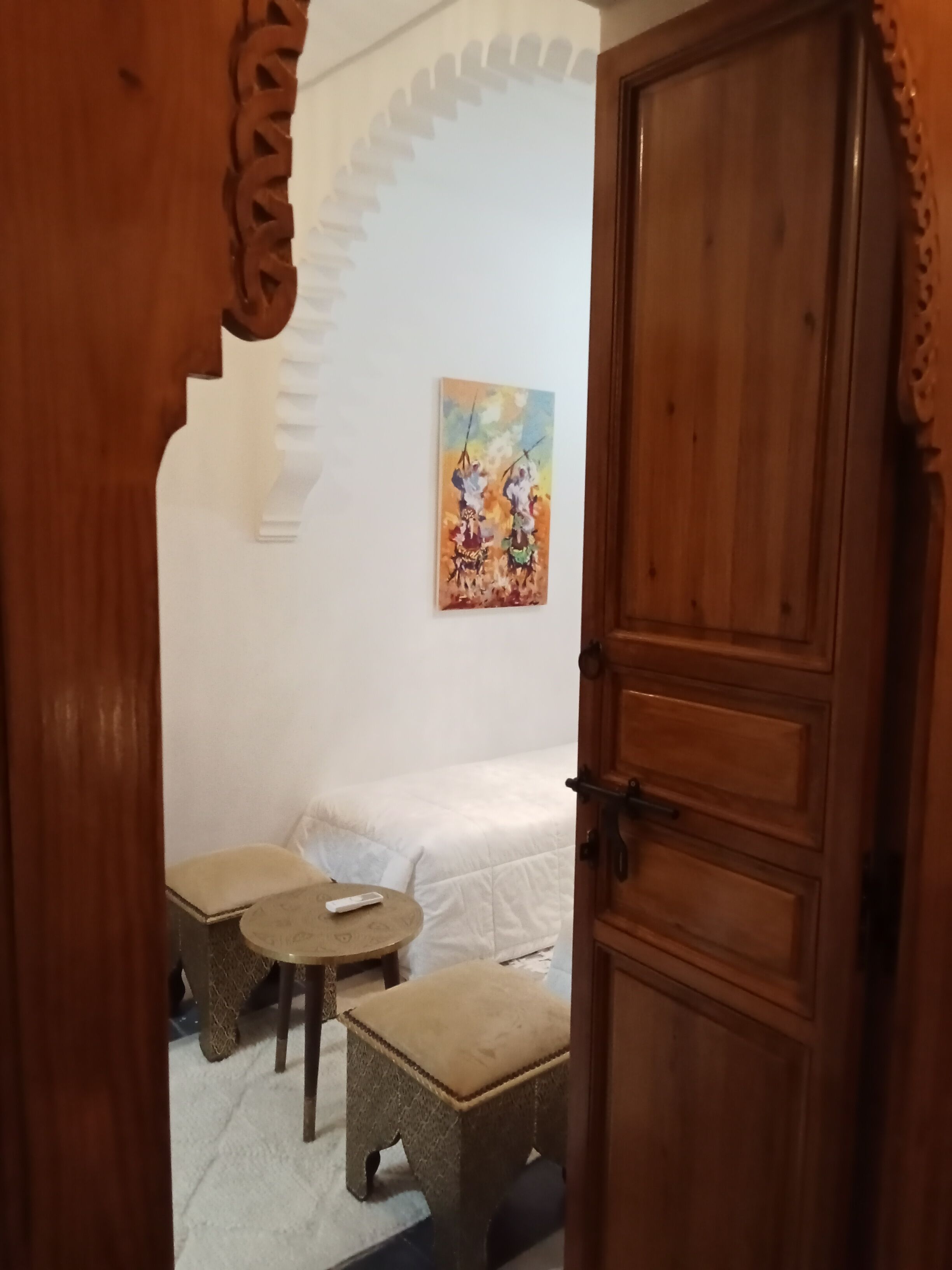 Ein Zimmer mit einem Bett, einem kleinen Tisch, einem Hocker und einem Bild an der Wand.