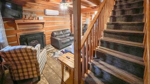 L’intérieur d’un chalet chaleureux, avec une cheminée, un canapé en cuir, un fauteuil à carreaux et un escalier.
