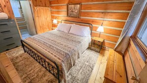 Une chambre à coucher dans un chalet en bois, avec un lit, deux lampes de chevet, une commode et une fenêtre.