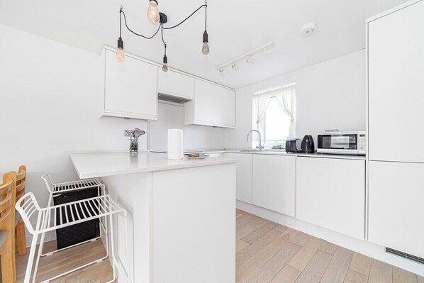 A modern kitchen with white cabinetry, a built-in microwave, and a hanging light fixture.