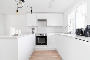A modern kitchen with white cabinetry, a built-in oven, a sink, and a window with sheer curtains.