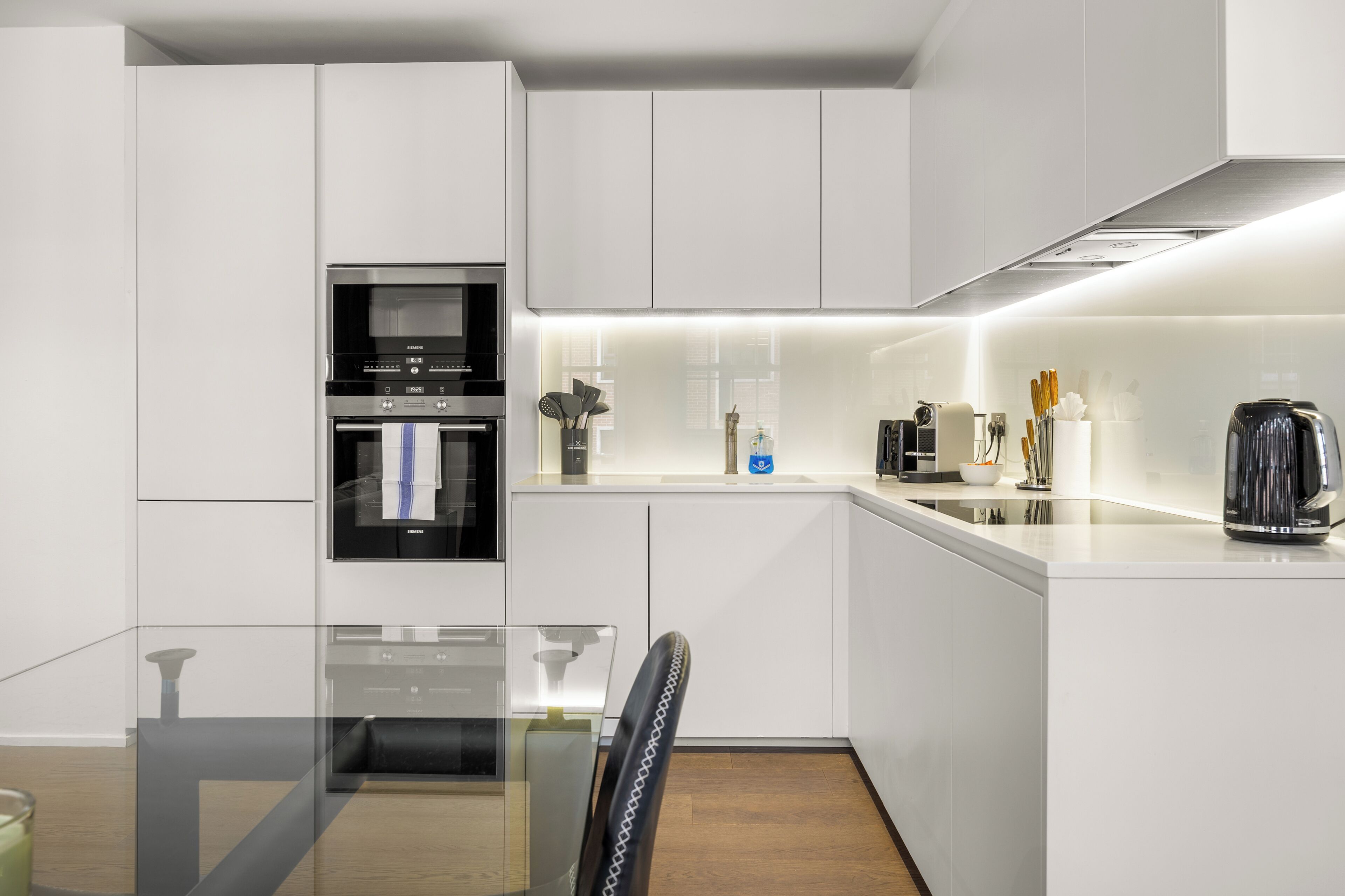 Una cocina moderna con armarios blancos, horno empotrado y cafetera.