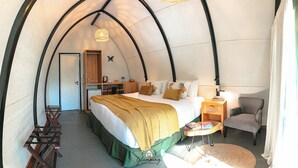 Una habitación acogedora de forma abovedada, con una cama, un escritorio, una silla y una pequeña mesa con libros.